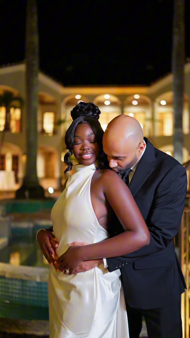 A couple in black tie and an ivory gown photographed at night beside the pool of a lit estate