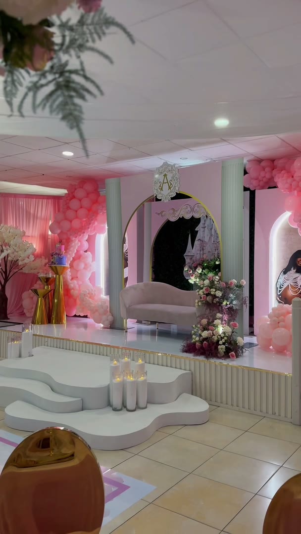 A ballroom dressed in pink for a princess themed baby shower, balloon arches and a castle backdrop, before any guest arrives