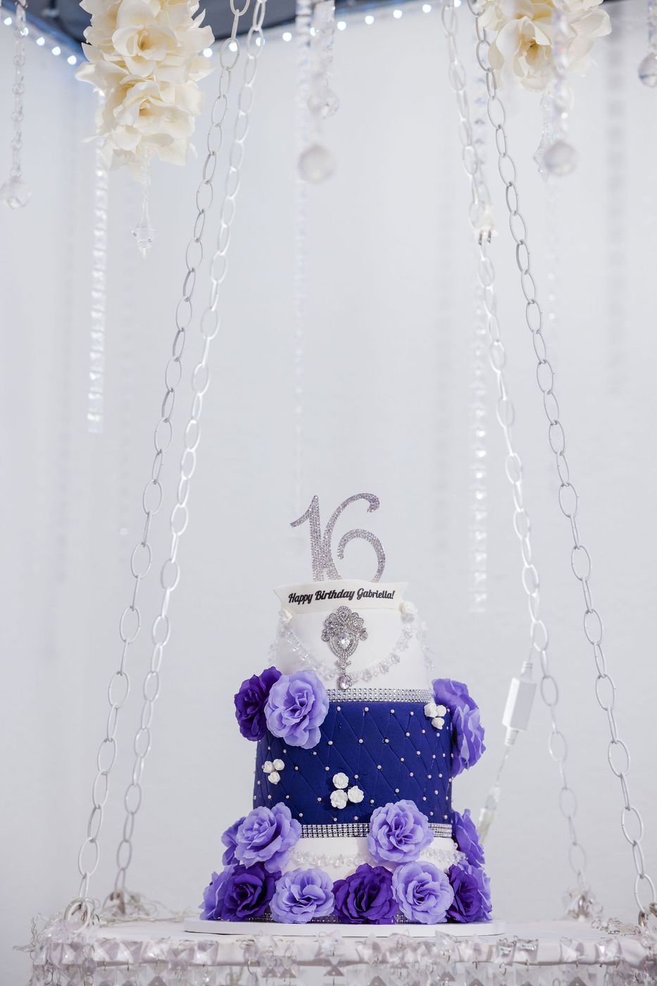 A navy and lavender sweet sixteen cake suspended beneath a curtain of crystals