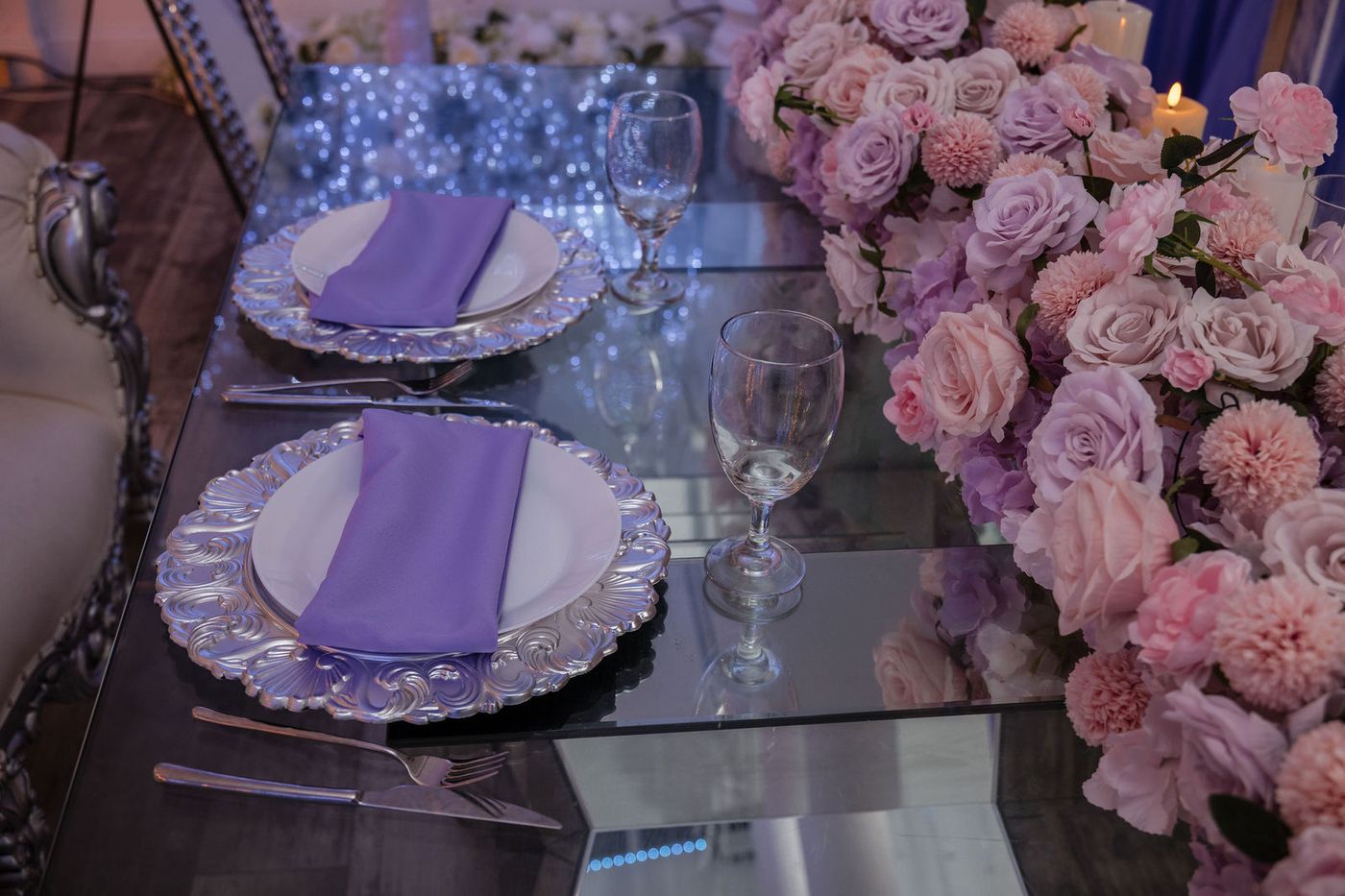 A place setting of lavender napkins and beaded chargers on a mirrored table