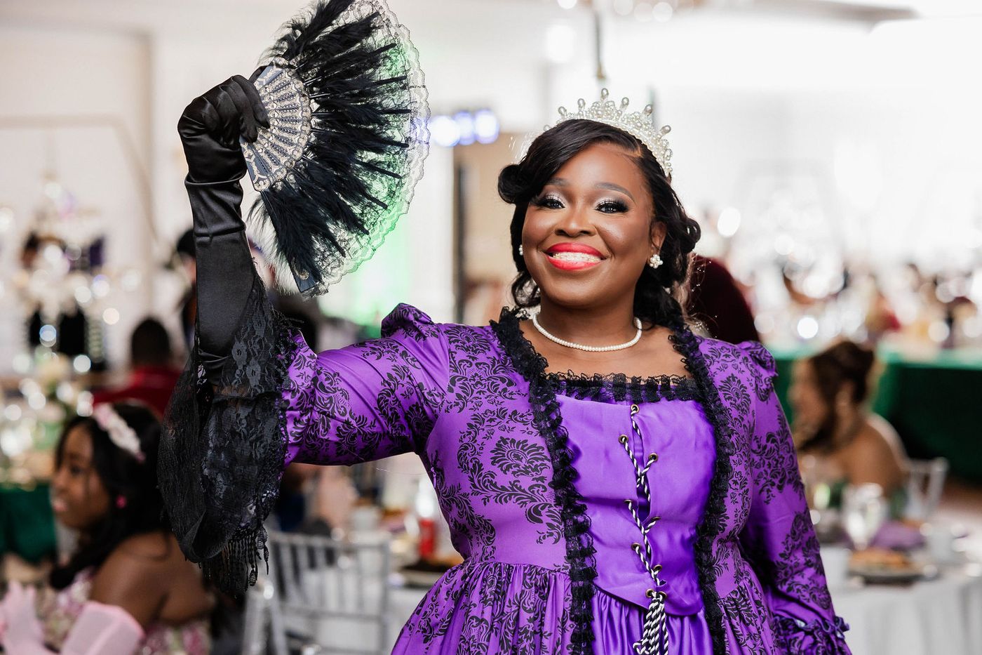 A guest in a purple period gown and tiara on the floor of a costume ball