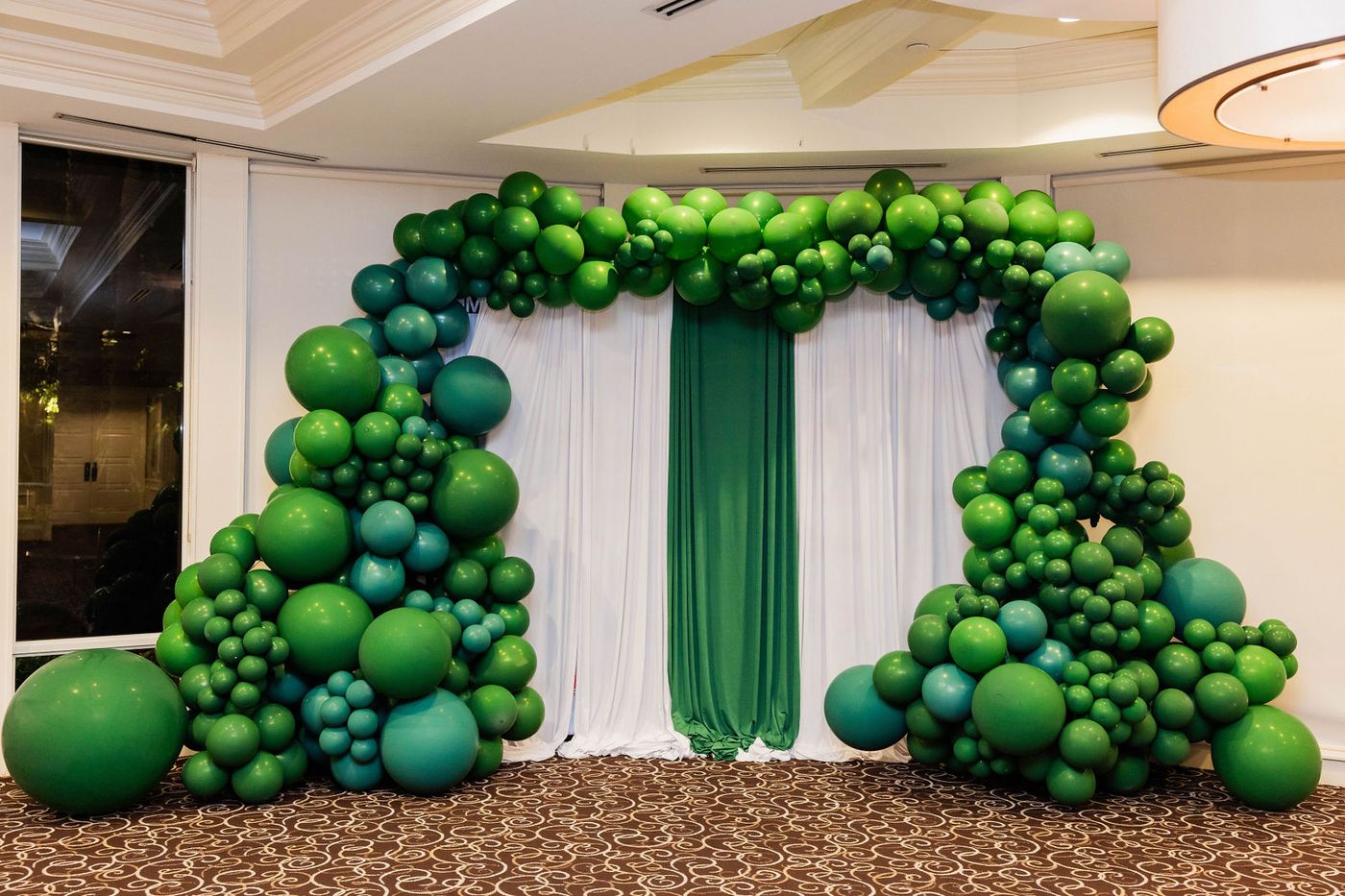 A green balloon arch and gold sequin backdrop at a themed ball