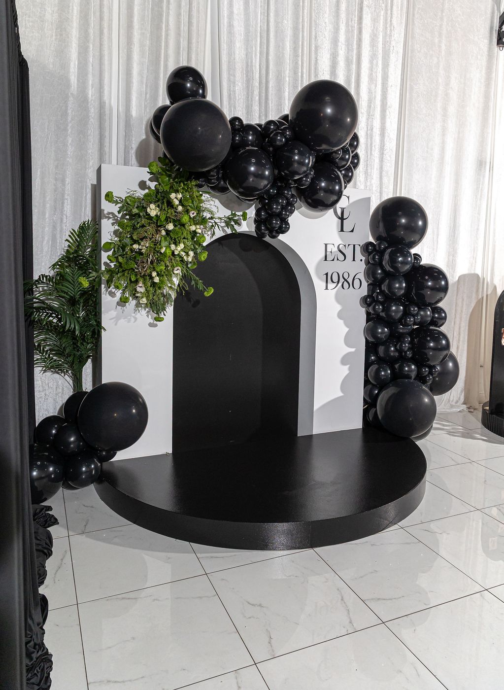 A black balloon arch framing a monogrammed milestone birthday backdrop