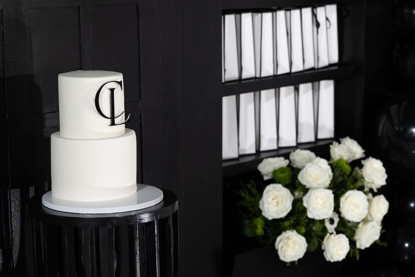 A white monogrammed cake on a black pedestal against a black wall