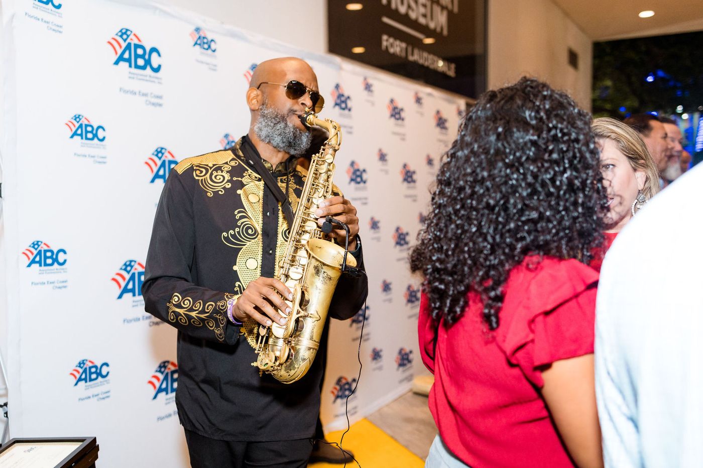 A saxophonist playing beside the sponsor backdrop at a corporate chapter mixer