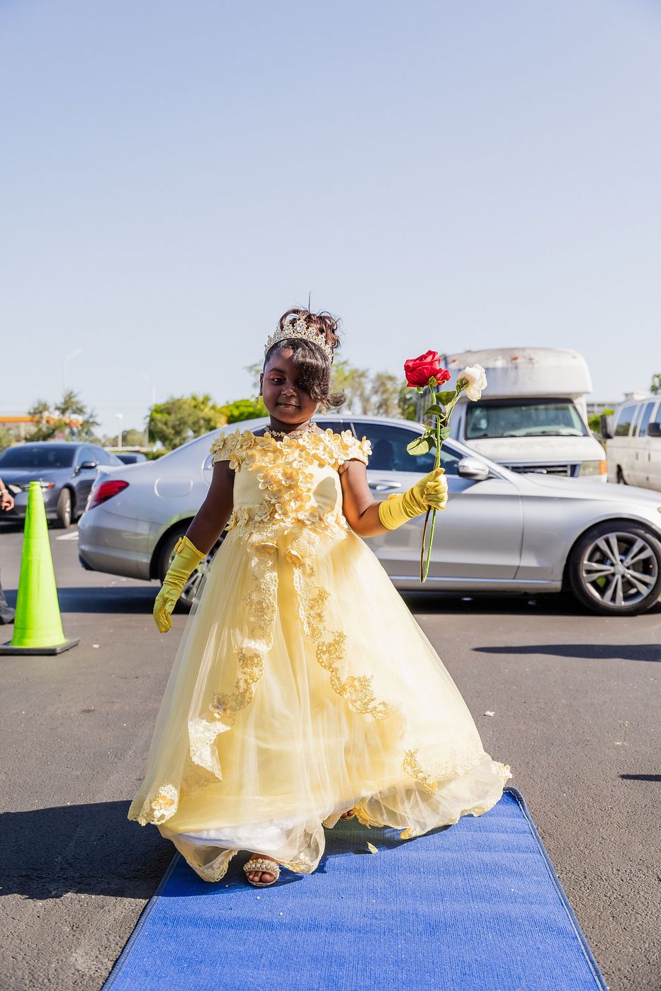 A child in a yellow ball gown walking the blue carpet at a kids' prom night