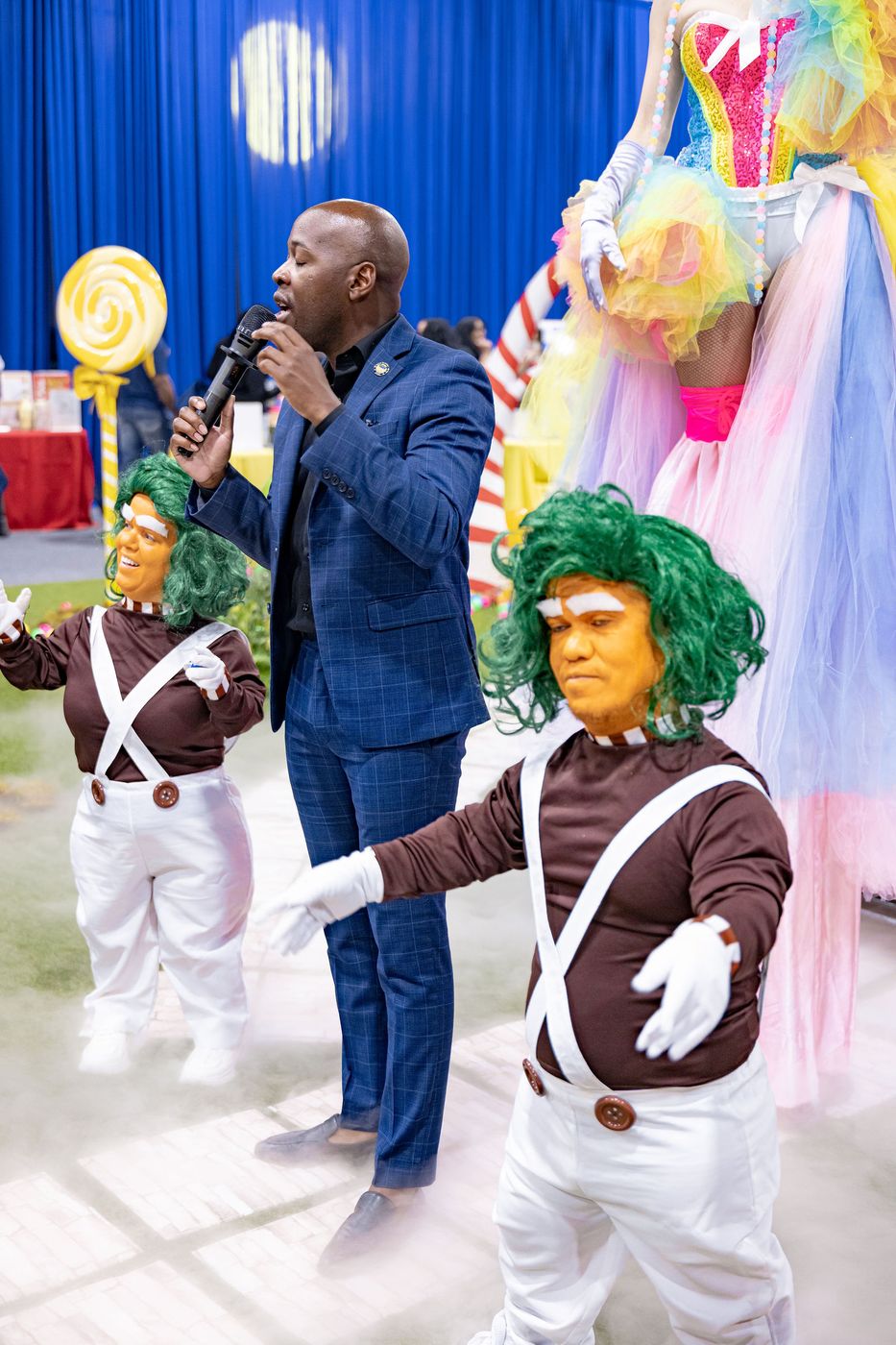 The host of a community event speaking beside two costumed characters
