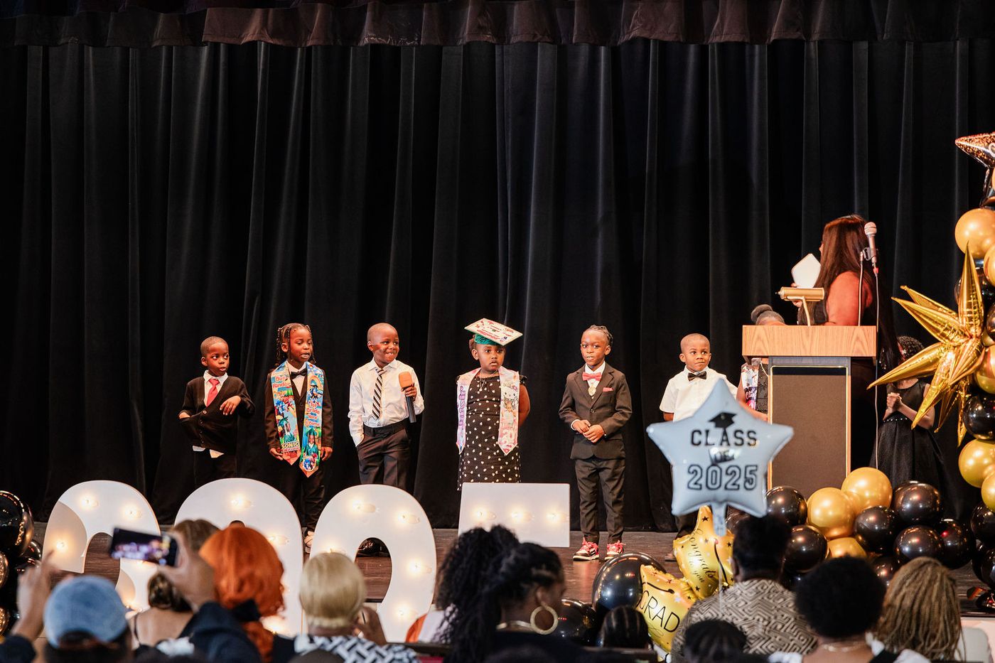 The graduating class on stage beside illuminated 2025 marquee letters