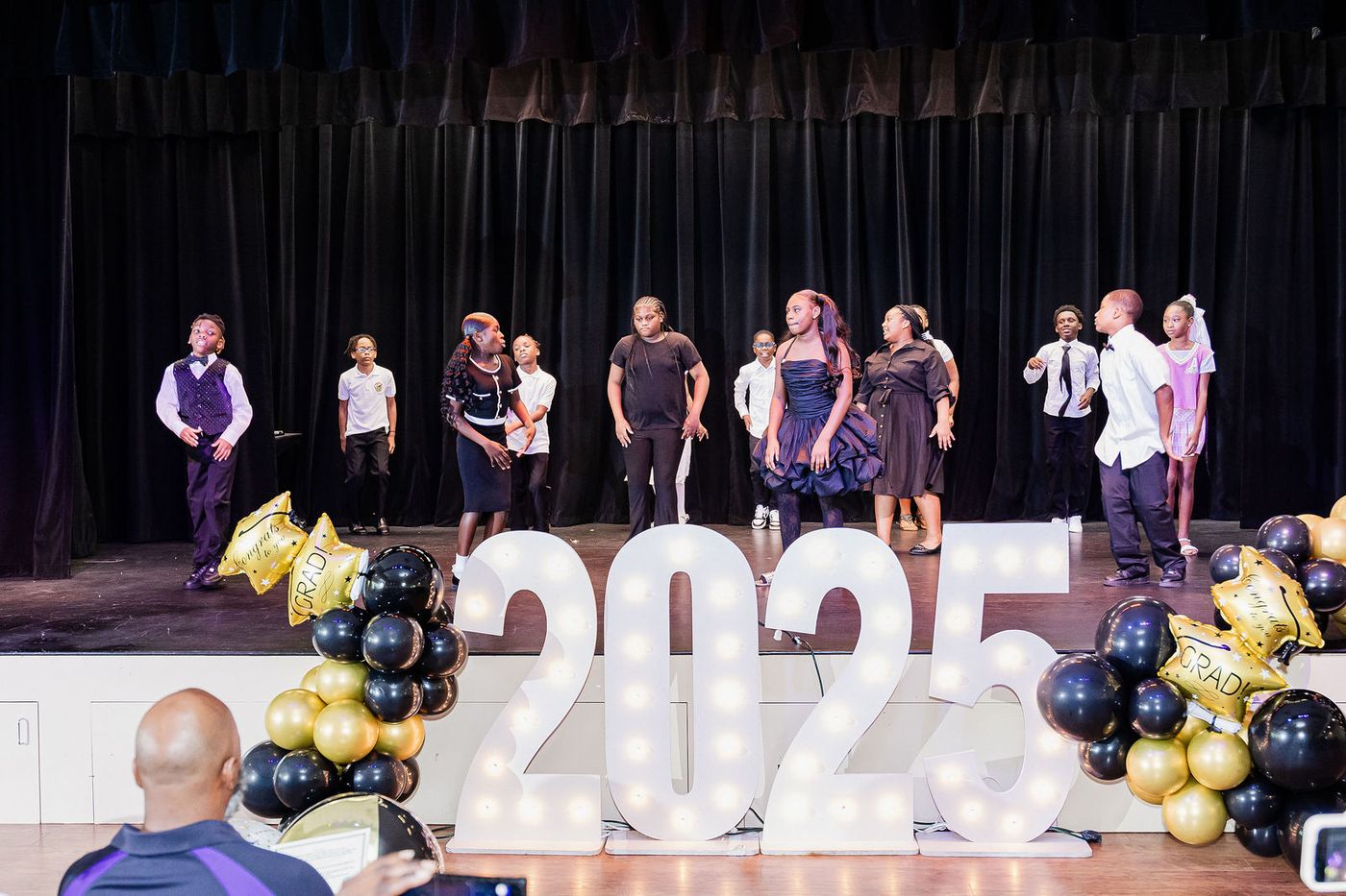 A class performance on stage in front of lit 2025 marquee letters