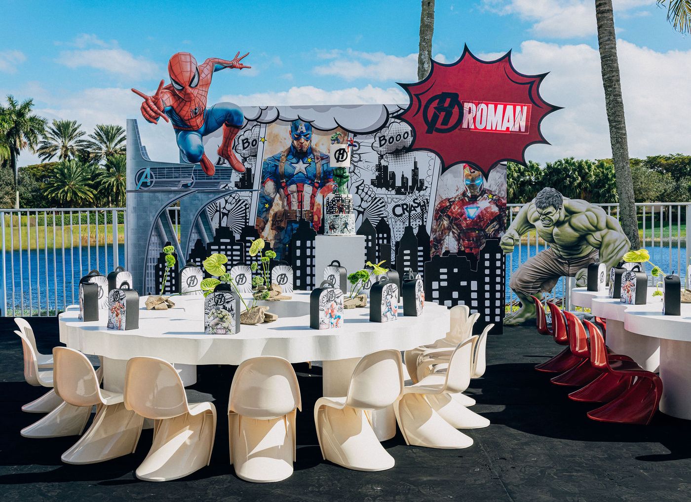 A comic-book themed children's birthday build beside a waterfront pool, laid with moulded chairs