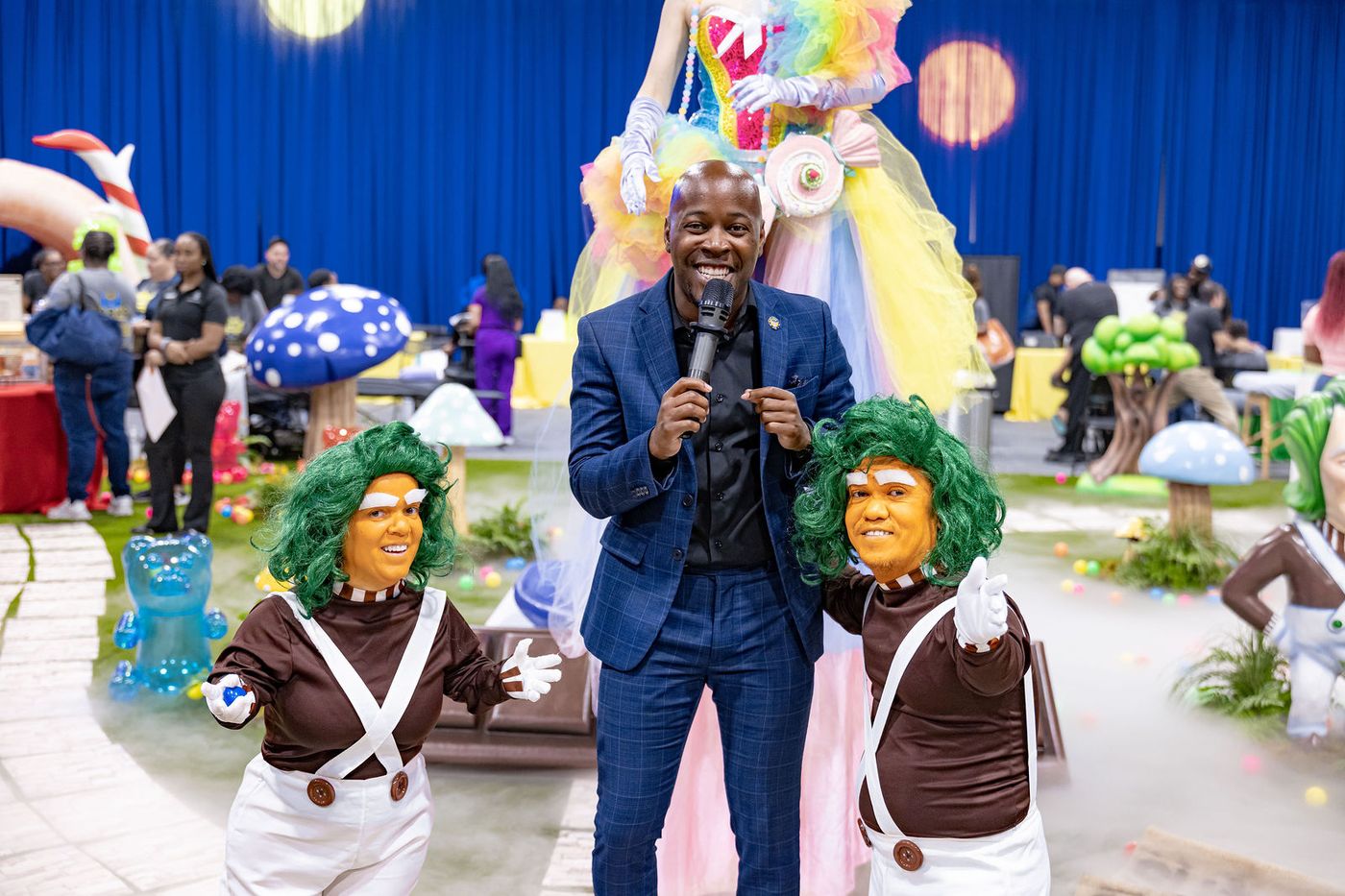 A wide frame of the host and performers on the floor of an immersive event