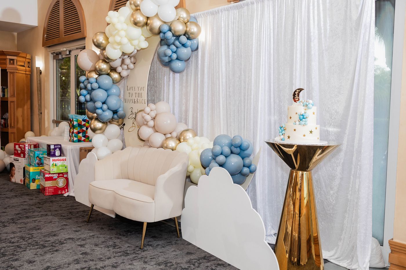 A baby shower cake on a gold pedestal beside the balloon arch