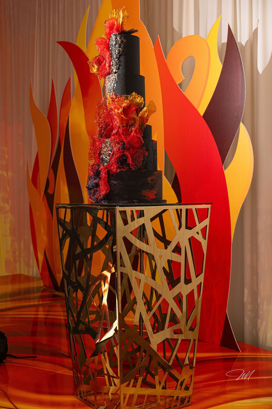 A tiered black cake trimmed with flame coloured sugar work at a milestone celebration