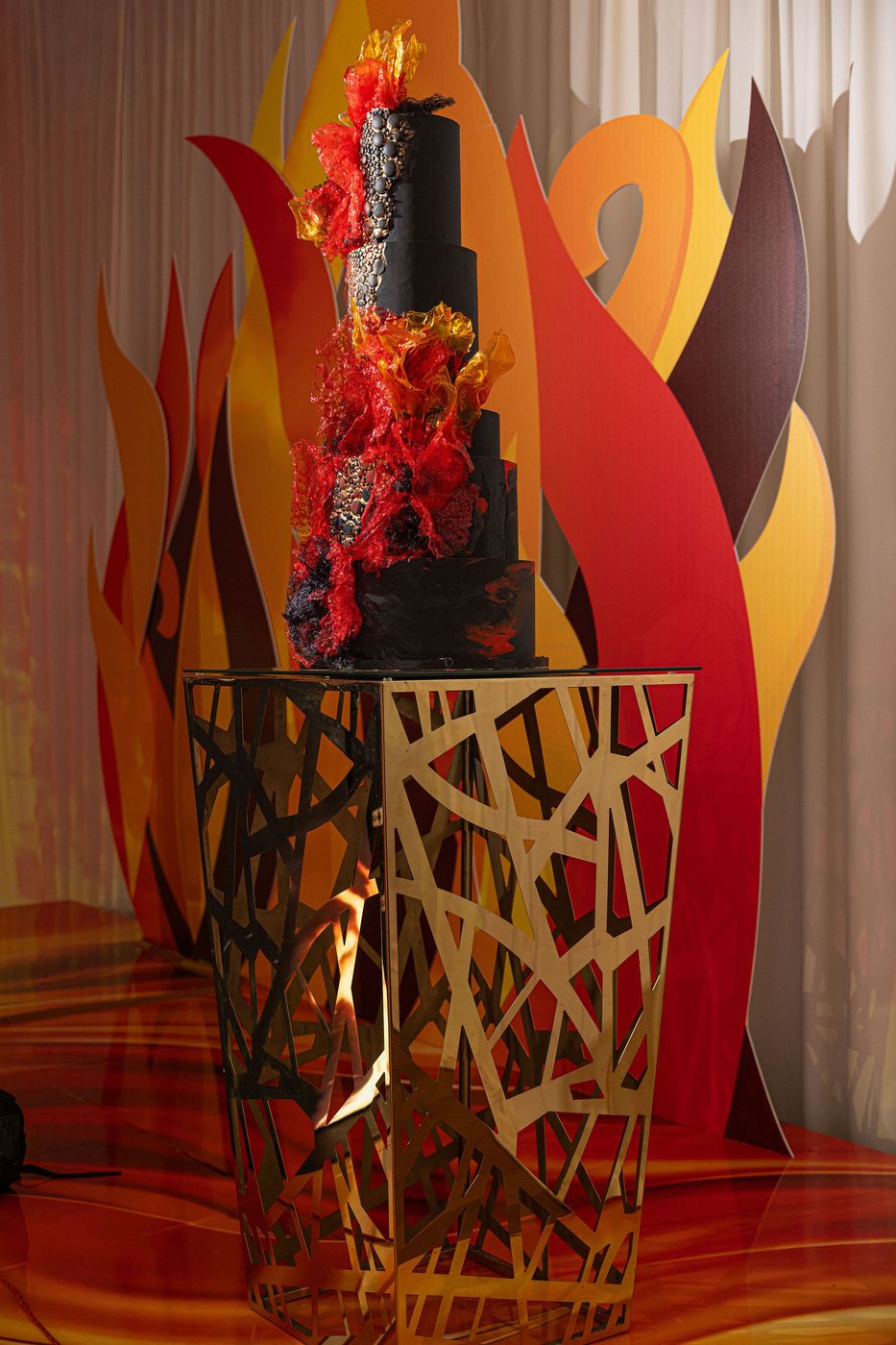 A black and flame coloured tiered cake on a sculptural gold stand