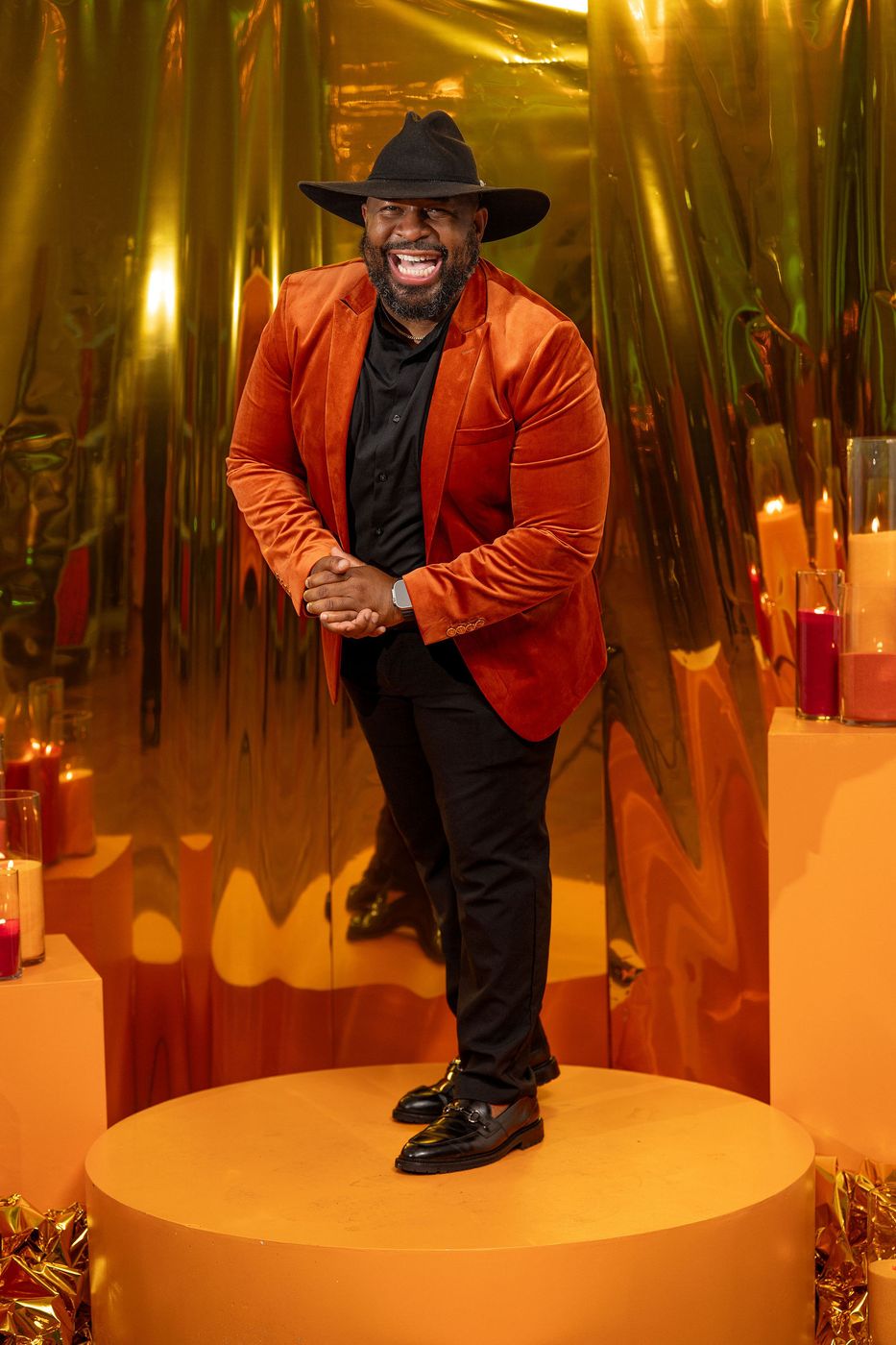 A guest in an orange velvet jacket and black hat at an evening celebration