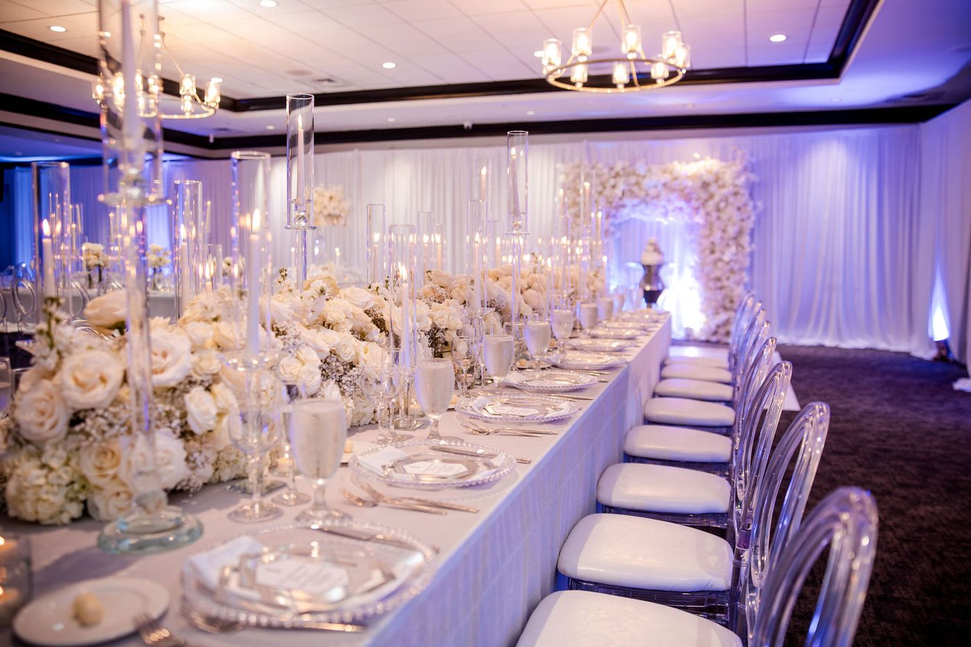 The head table of an anniversary gala, white florals running its full length under blue uplight