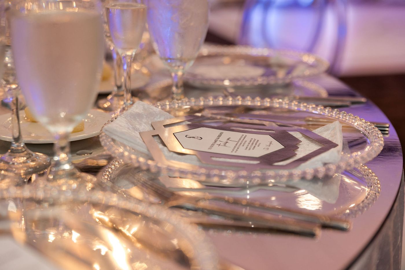 A candlelit place setting at an anniversary gala, glassware catching the warm light