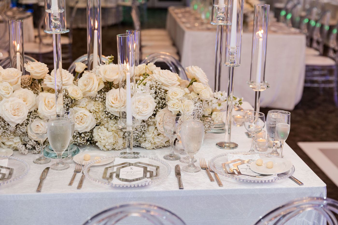 A low centrepiece of white roses and hydrangea between tall tapers on a banquet table