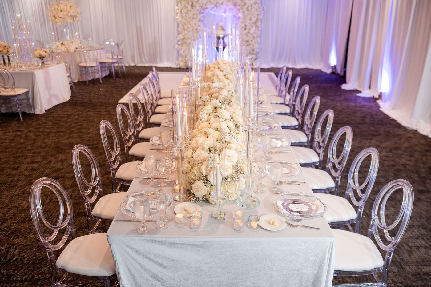 Tall glass candlesticks and a white floral centrepiece down a mirrored banquet table