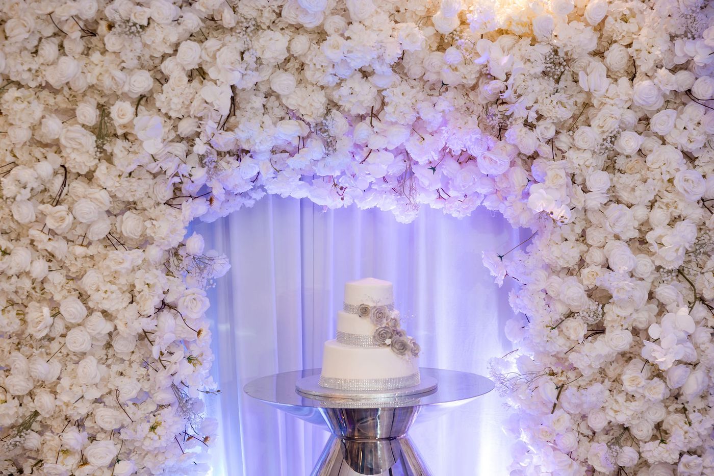 A cake stand set against a wall of white roses at an anniversary gala